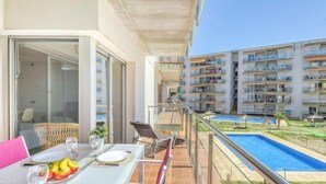 Un balcón con una mesa y sillas dispuestas, una piscina y vistas de edificios de apartamentos cercanos.