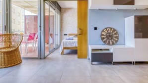 Una habitación de hotel moderna con un armario de cristal corredera que da a una zona de estar al aire libre, una cama con cabecera de madera y un reloj de pared grande.
