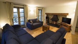 Una sala de estar con un sofá, televisor, chimenea y un amplio ventanal con cortinas.