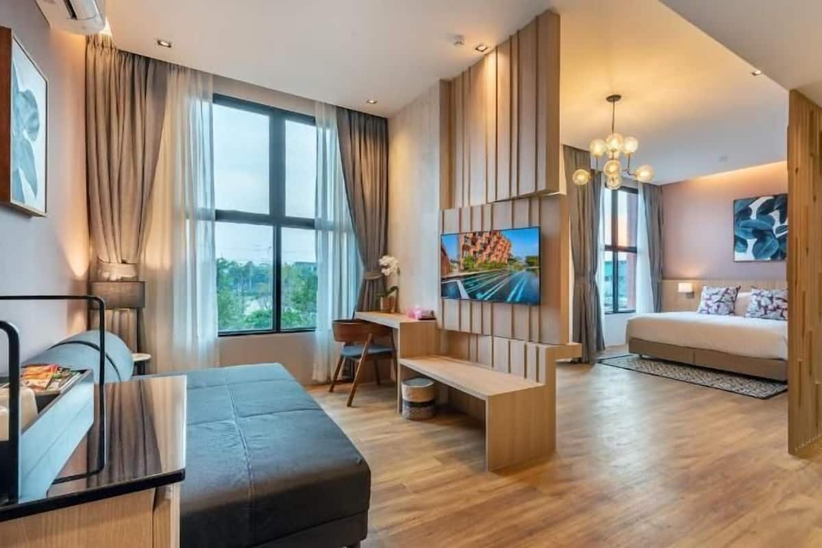 A modern hotel room with a large window, a flat-screen TV, a sofa, a desk, and a bed.