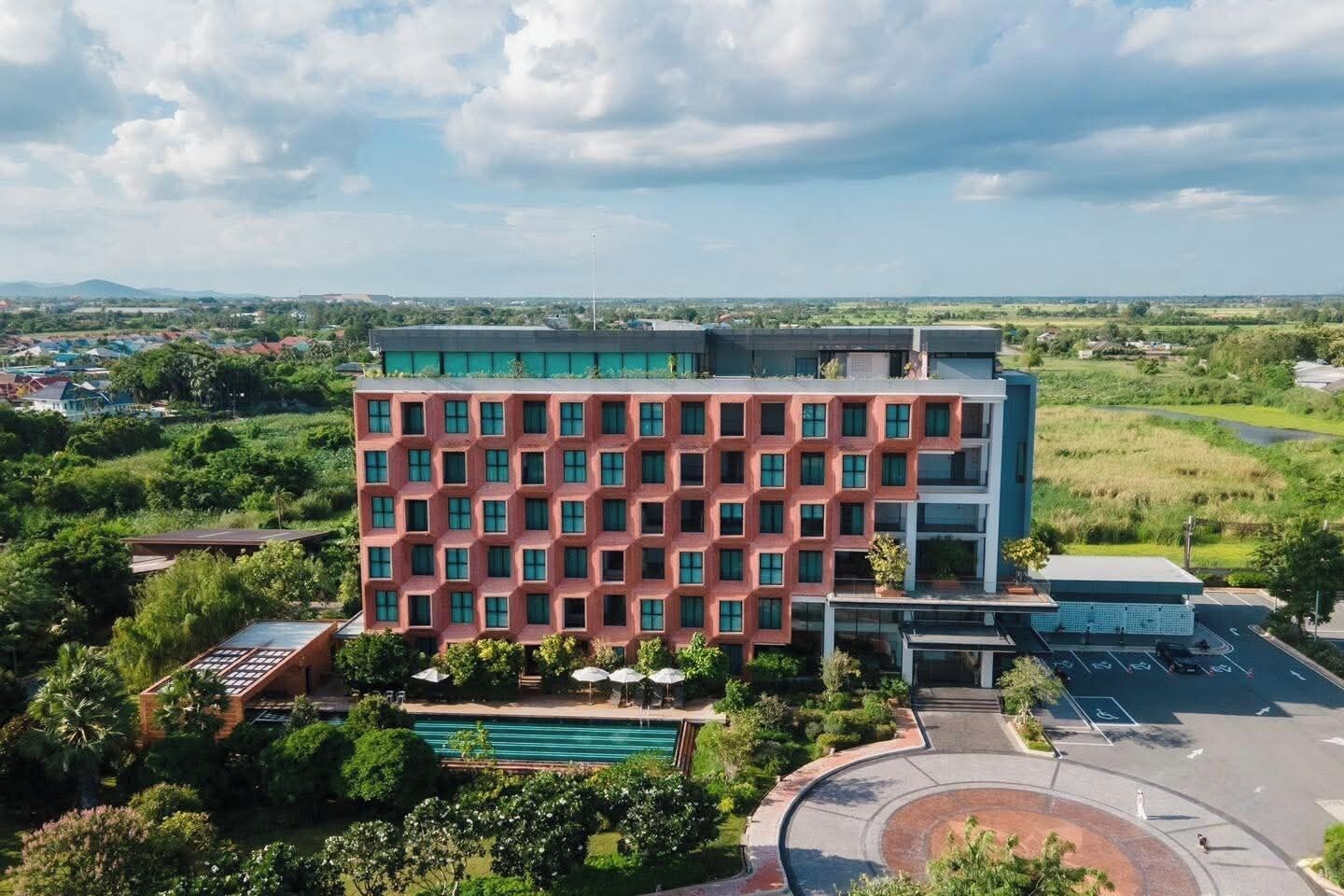 A multi-story hotel with a red facade, surrounded by greenery and a swimming pool.