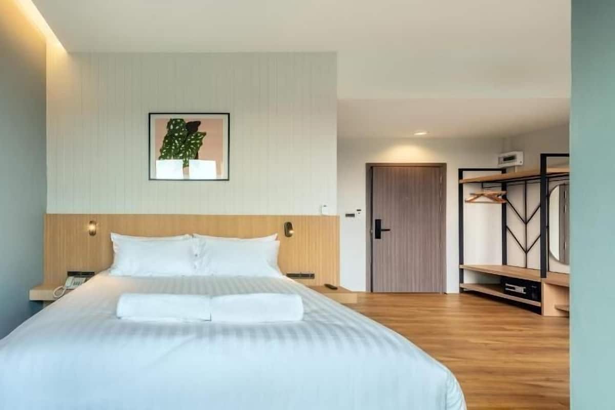 A modern hotel room with a large bed, a wooden headboard, a framed picture on the wall, and a wardrobe with a mirror.