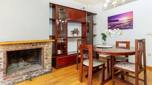 Un coin repas agrémenté d’une cheminée en briques, de chaises en bois, d’une table ronde et d’un lustre moderne.