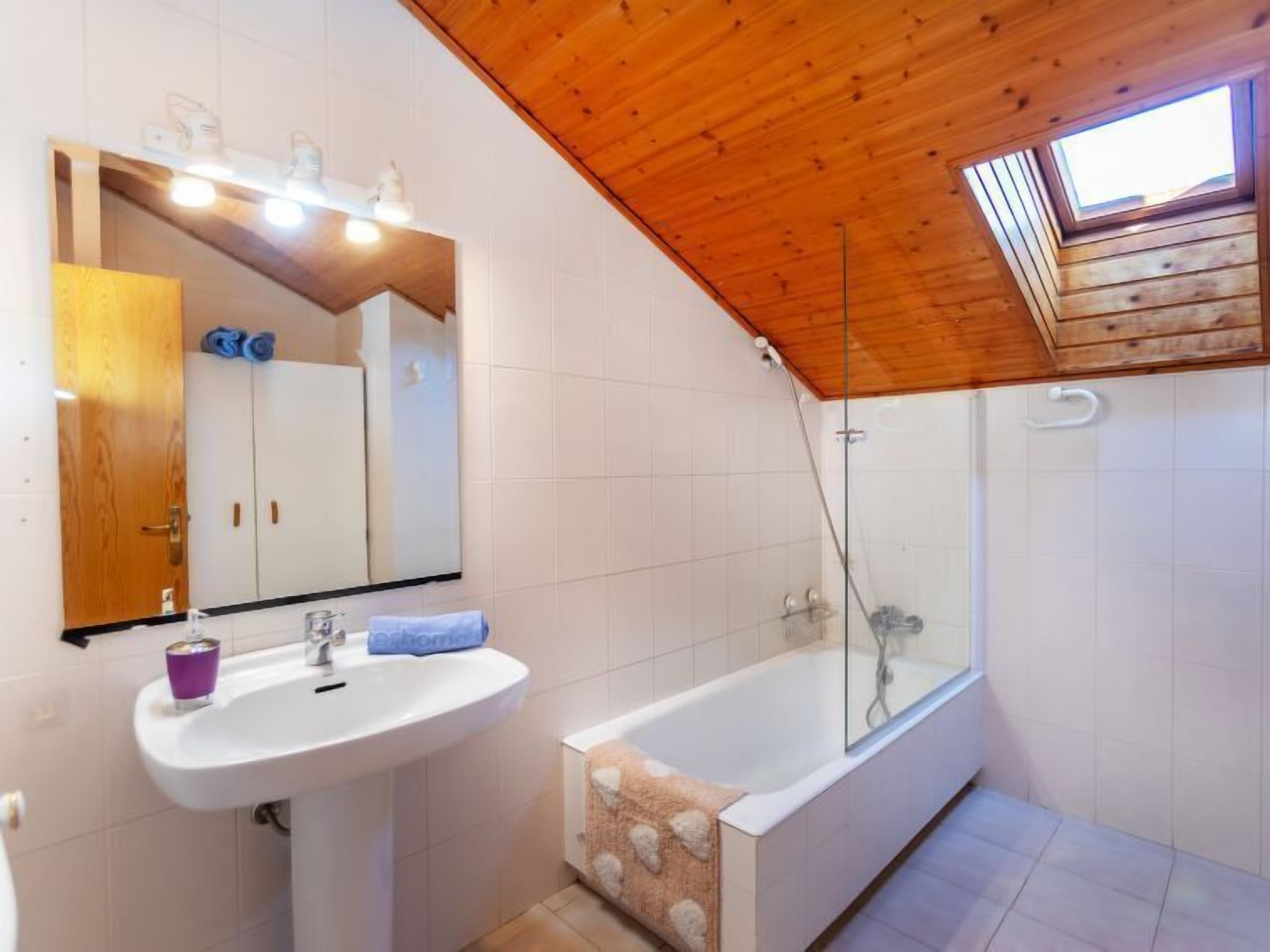 Ein modernes Badezimmer mit Holzboden, einem großen Spiegel, einem Waschbecken, einer Badewanne und einer Dusche.
