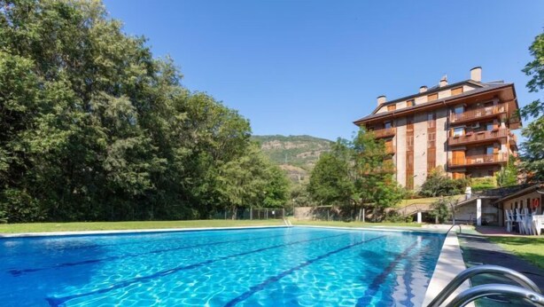 Une piscine à l’eau d’un bleu cristallin, entourée d’une végétation luxuriante et bordée d’un immeuble à plusieurs étages doté de balcons.