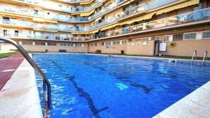 Ein Schwimmbecken mit klar blauem Wasser, umgeben von einem mehrstöckigen Gebäude mit Balkonen.