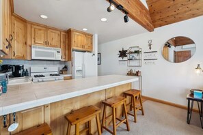 Une cuisine avec des meubles de rangement en bois, un plan de travail blanc, une cuisinière et des tabourets de bar.