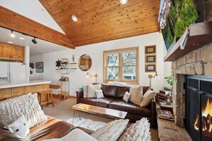 Un salon chaleureux avec une cheminée, un plafond en bois et une vue sur un paysage montagneux.