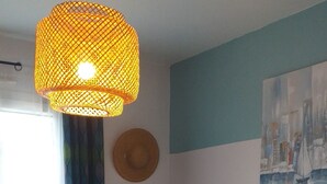 A bedroom with a bed, a hanging light, a painting, and a window with curtains.