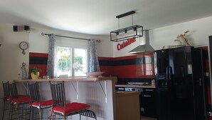 A kitchen with a dining area, a clock, a bookshelf, and a refrigerator.