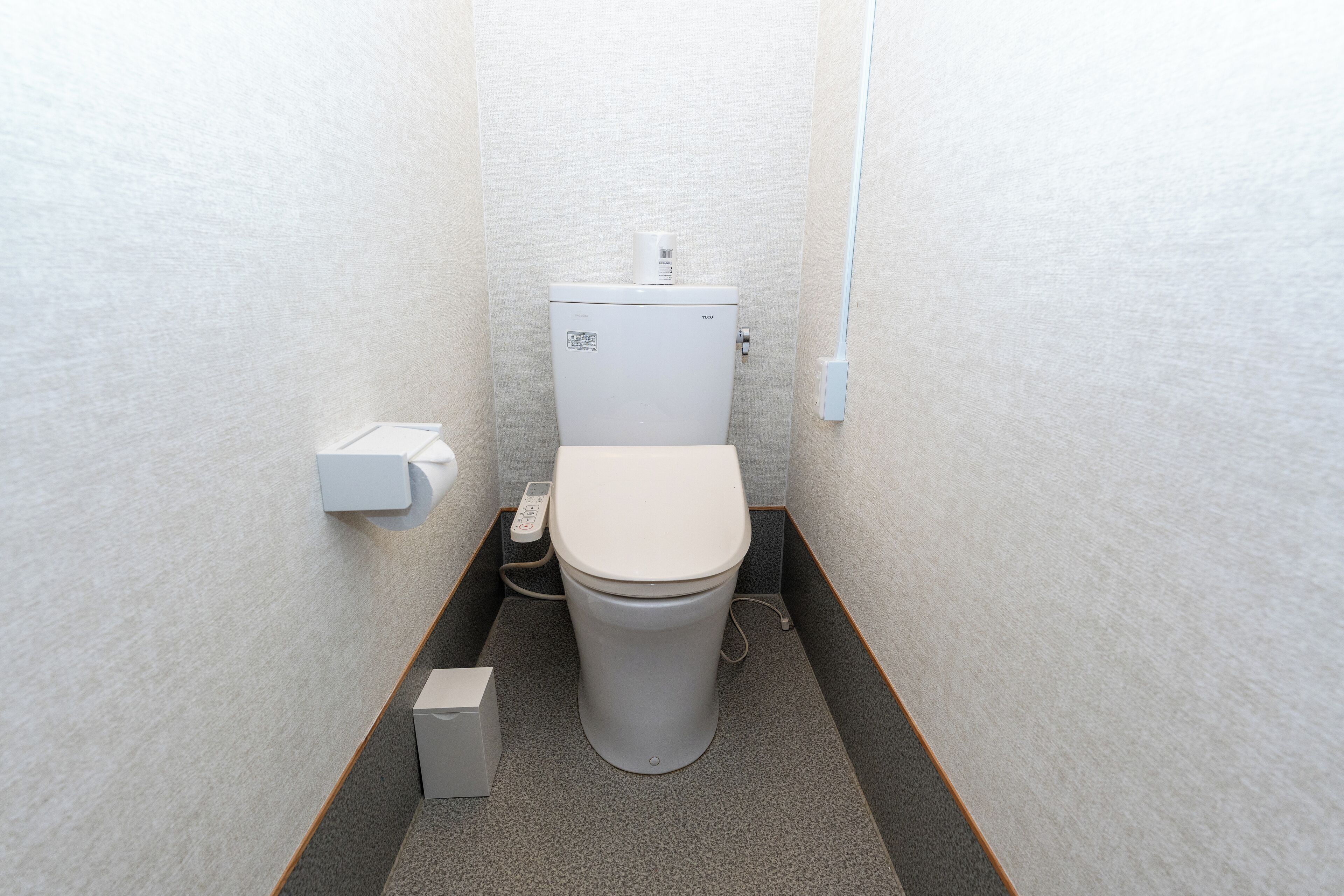 A small, compact bathroom with a toilet, a hand dryer, and a trash bin.