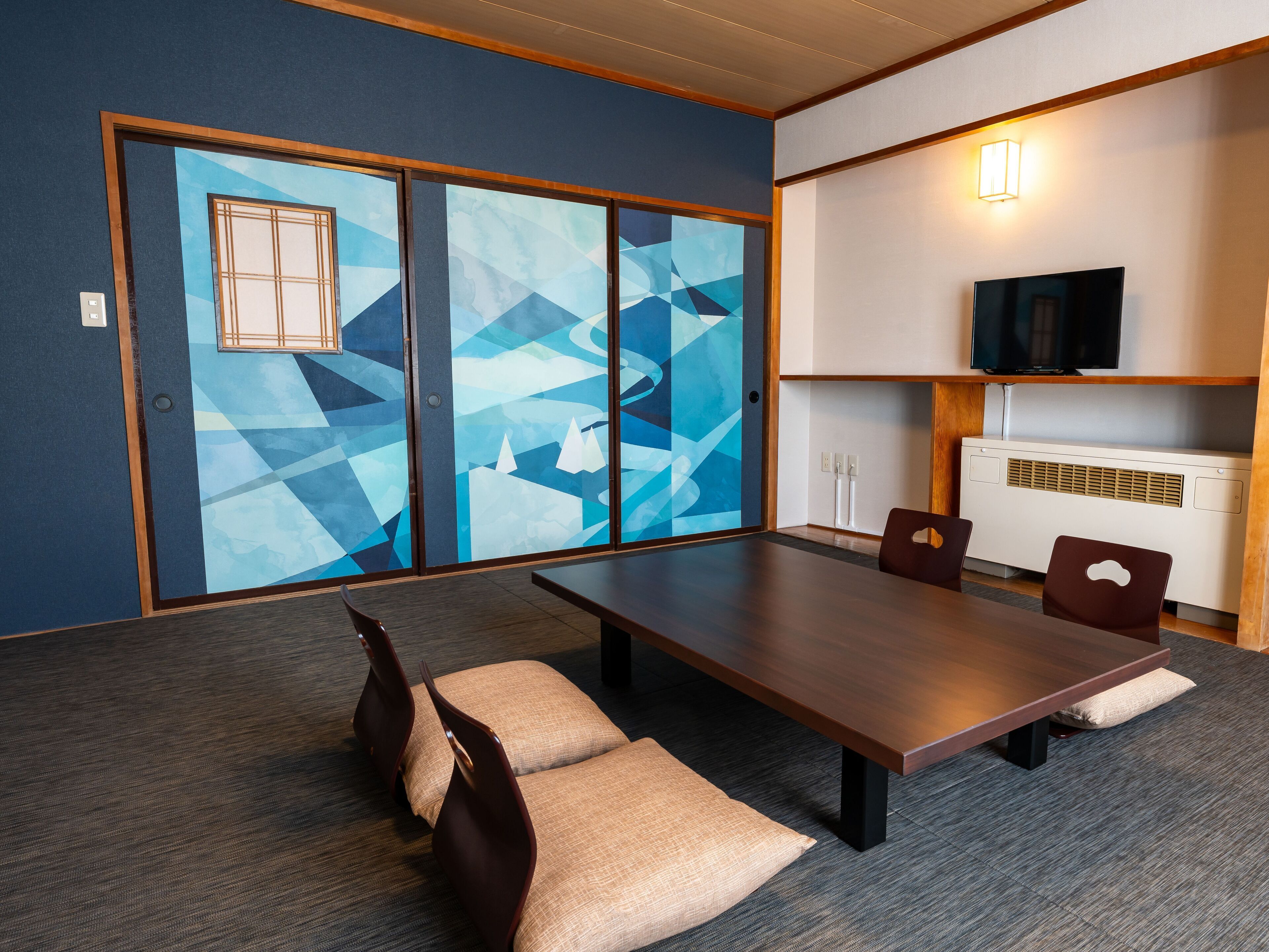 A conference room with a long table, two chairs, a television, and a wall-mounted heater.