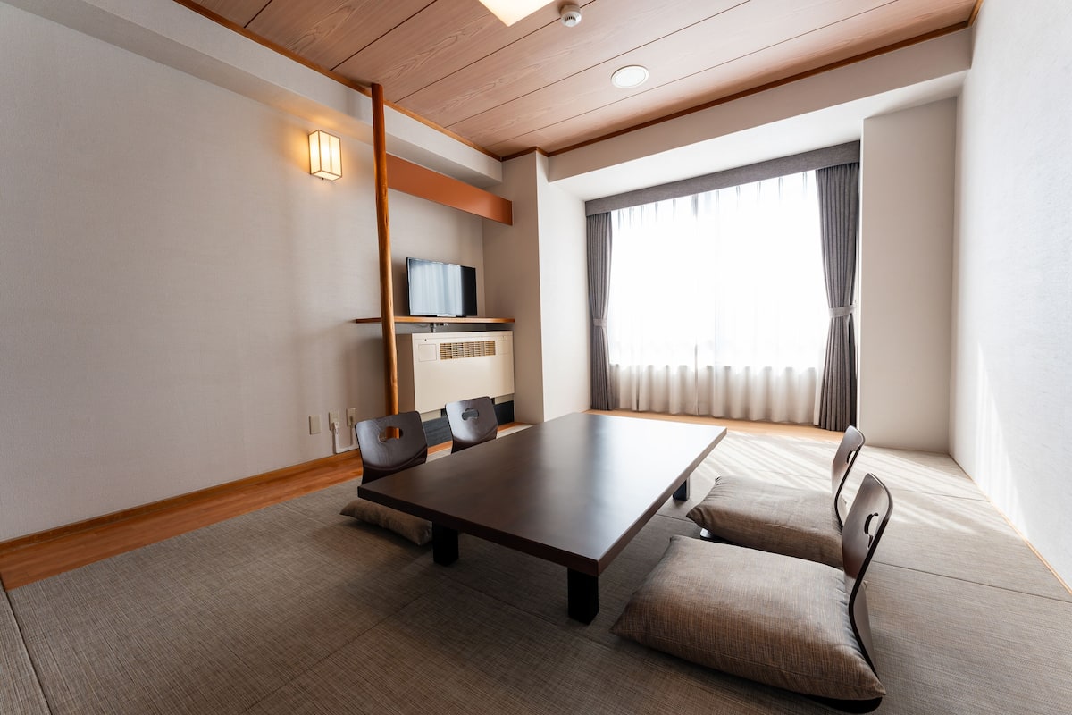 Ein modernes Hotelzimmer mit einem großen Bett, einem Nachttisch, einem Flachbildfernseher und einem Fenster mit Vorhängen.