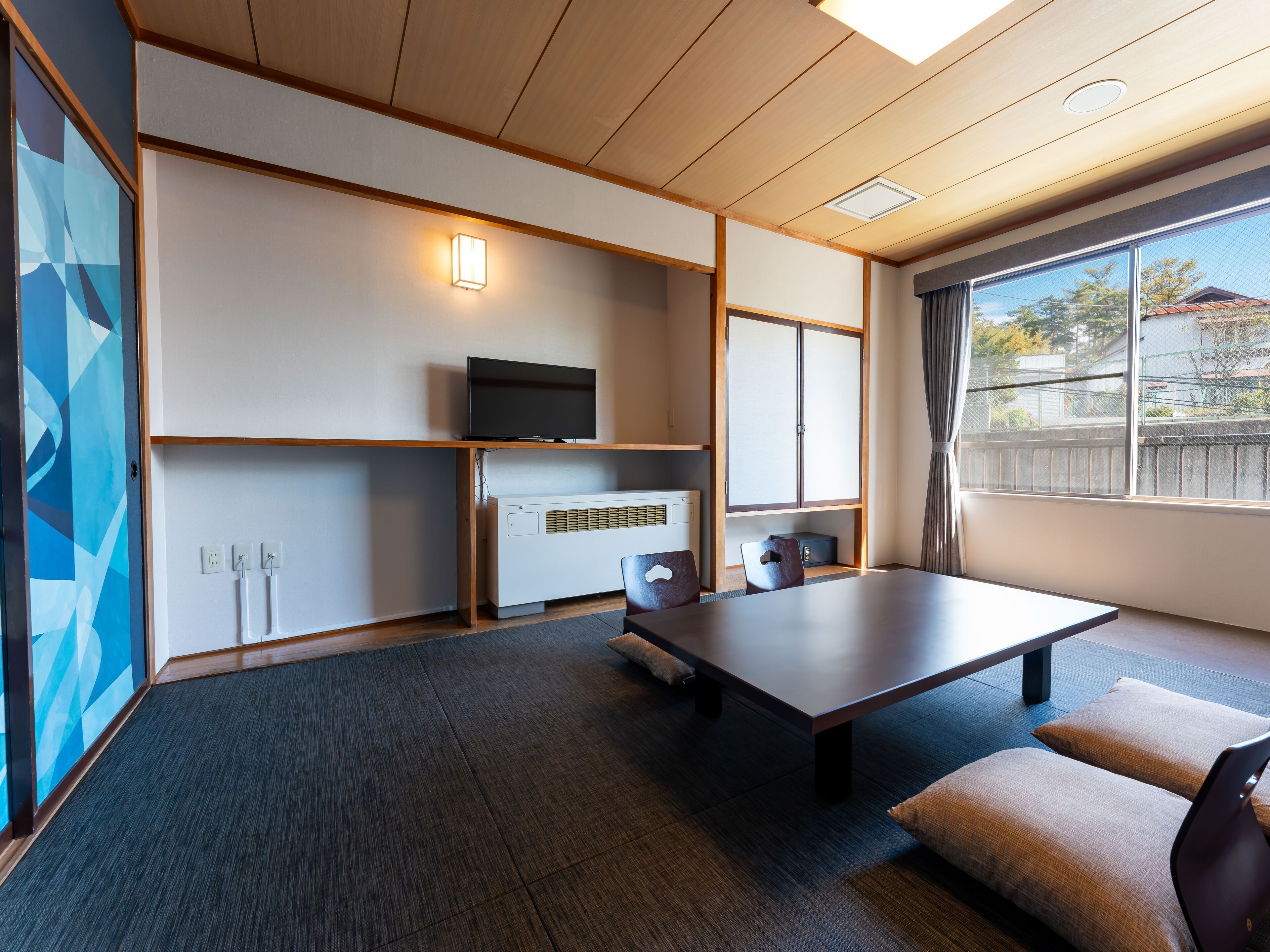 A modern room with a large table, a flat-screen TV, a heater, and a window with a view of the outside.