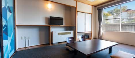 A modern room with a large table, a flat-screen TV, a heater, and a window with a view of the outside.