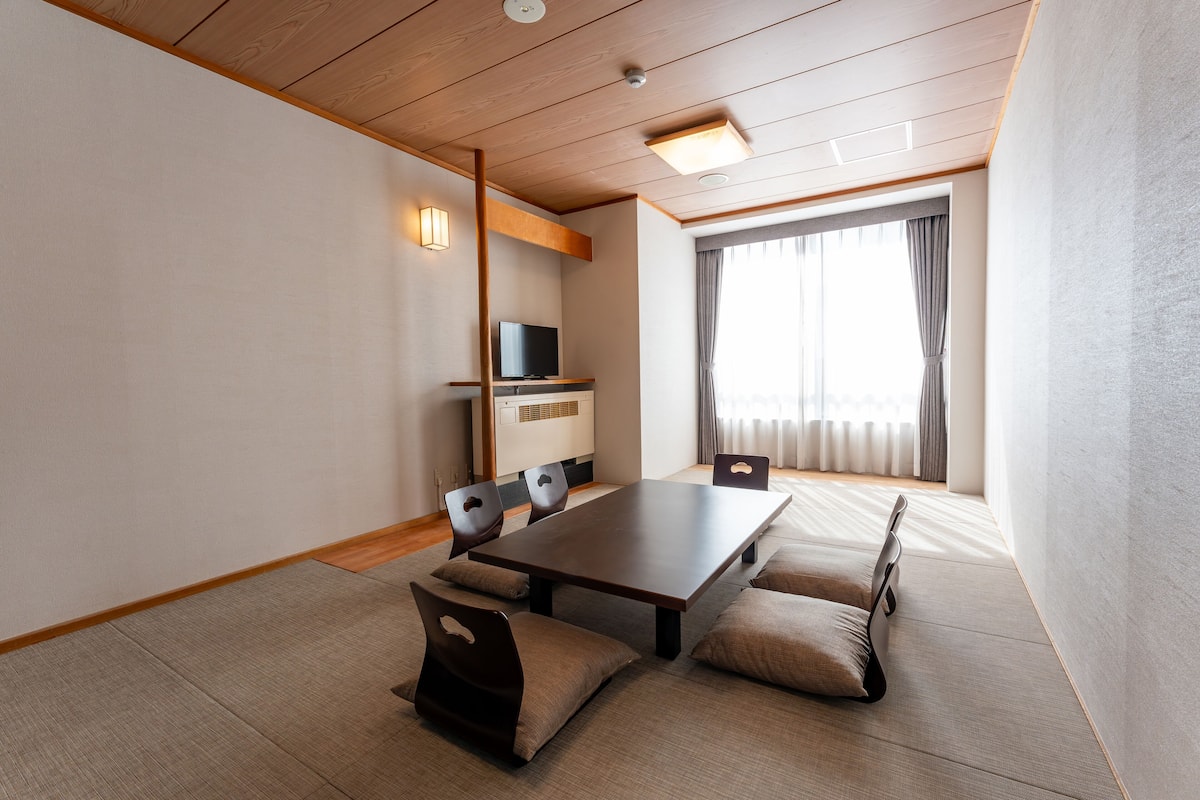 Ein modernes Hotelzimmer mit Holzboden, einem großen Esstisch und einem Fernseher.