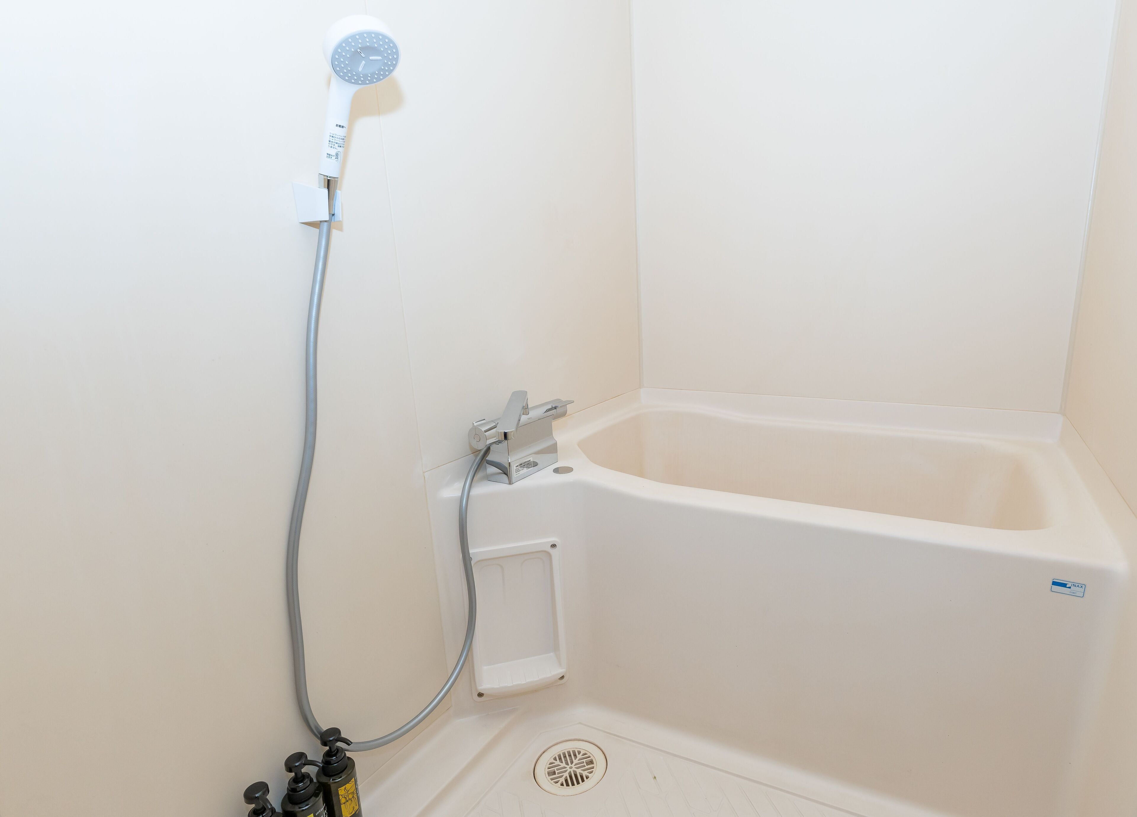 Une baignoire blanche dotée d’un pommeau de douche à main, d’un petit panneau de commande et d’un drain.