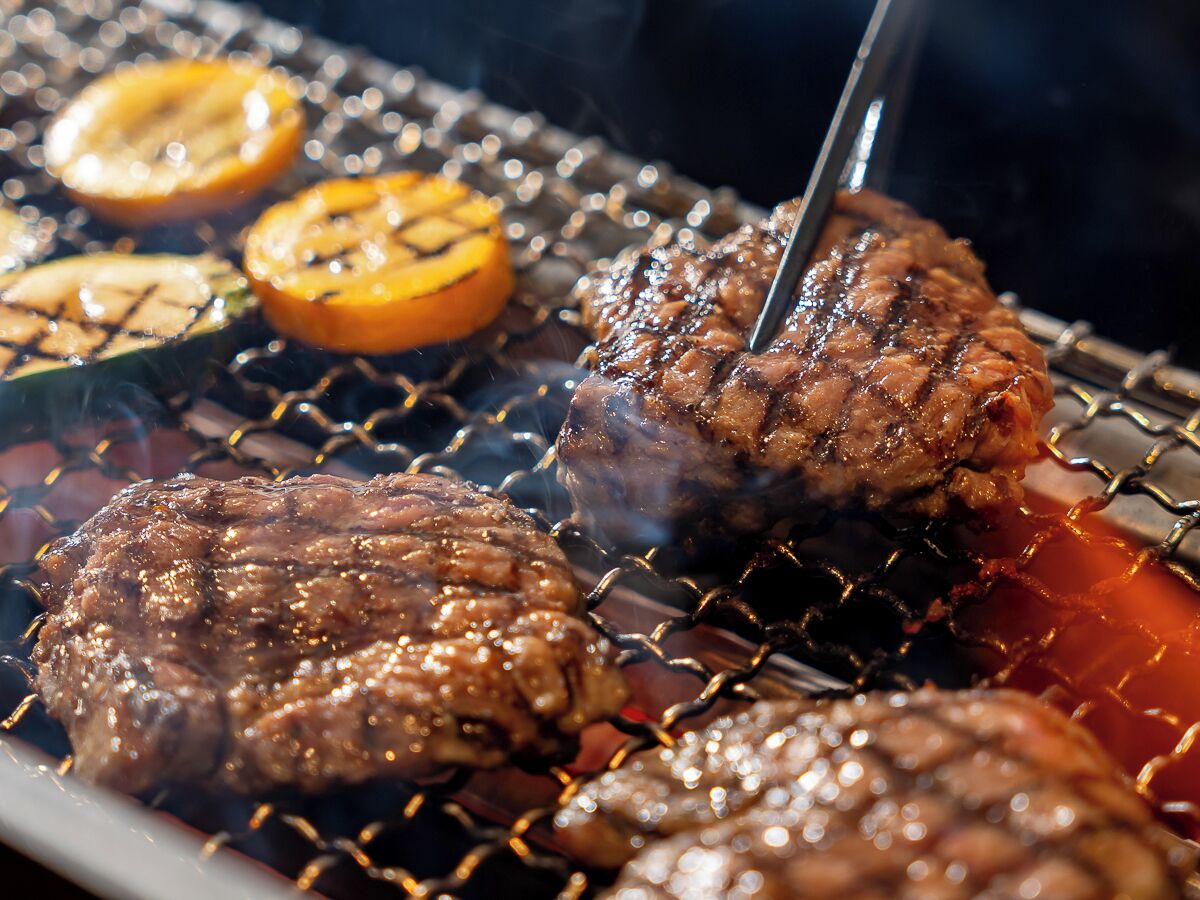A grill with burgers and sliced vegetables.