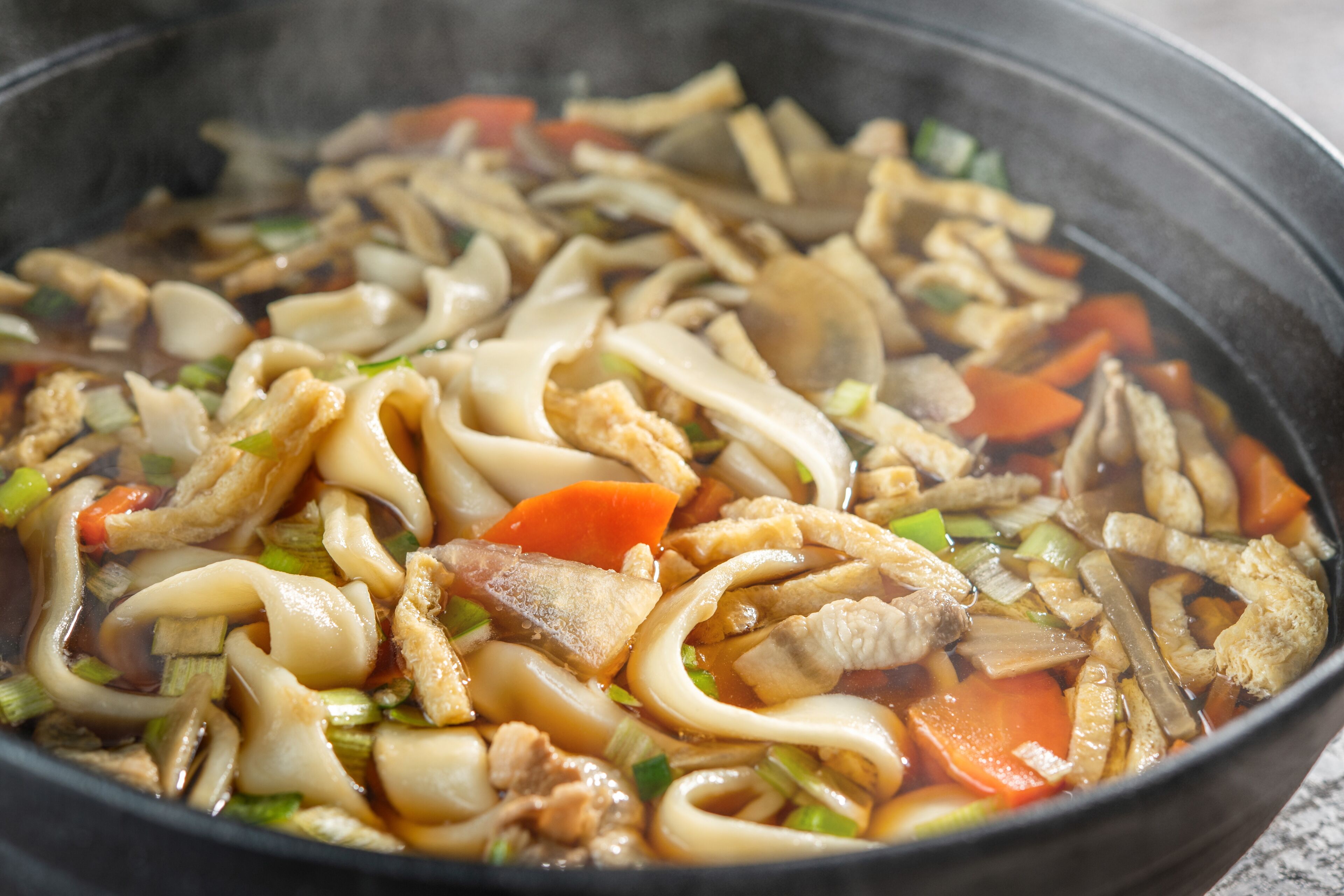 A close-up of a stir-fried noodle dish with vegetables and meat in a pan.