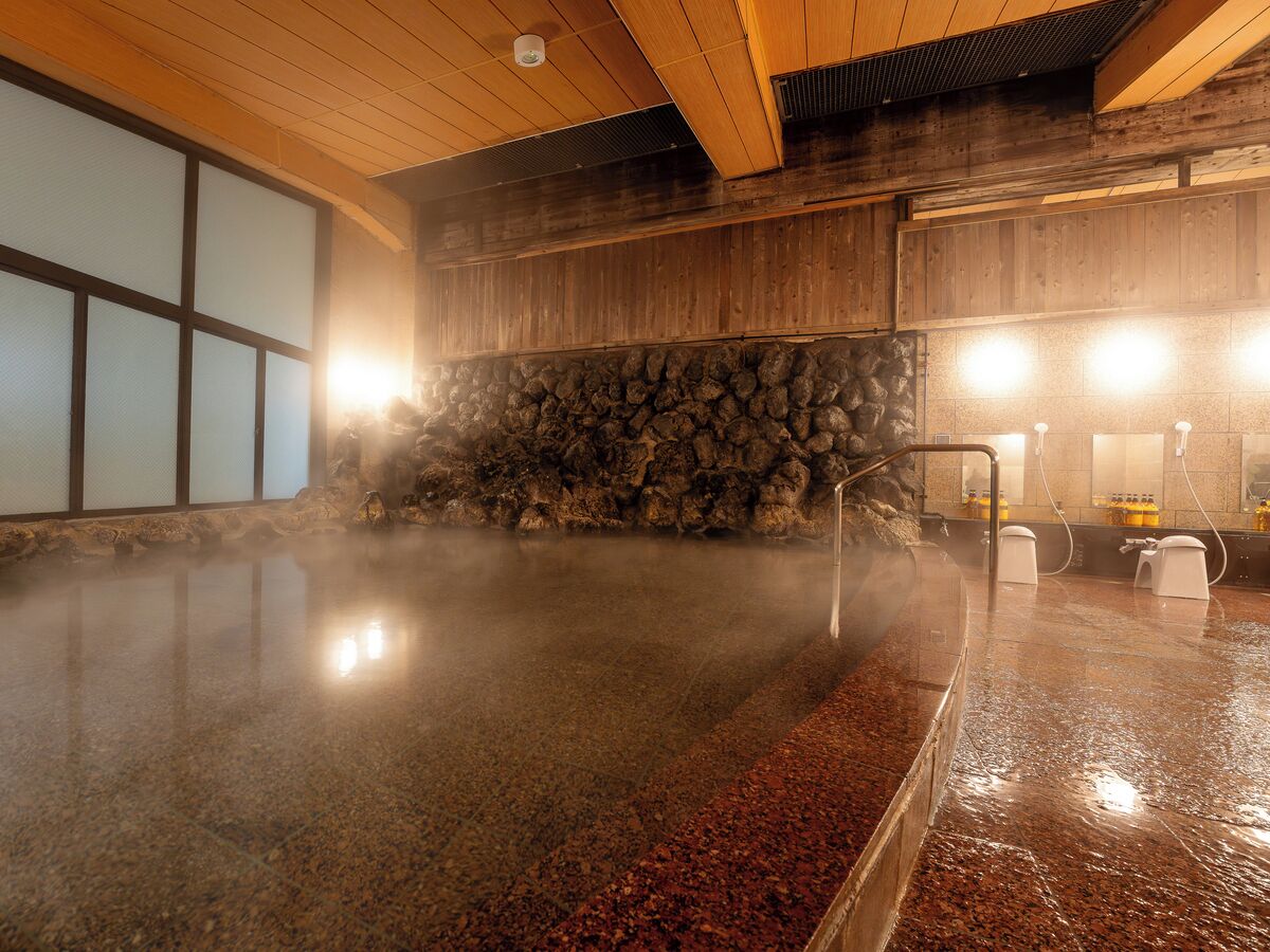 A hot spring bath with a stone wall backdrop and a wooden ceiling.