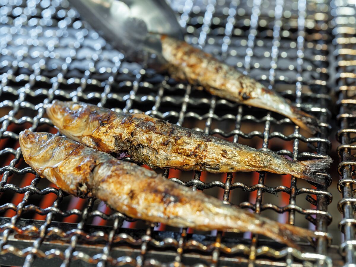 Tres pescados a la parrilla sobre una rejilla de metal.