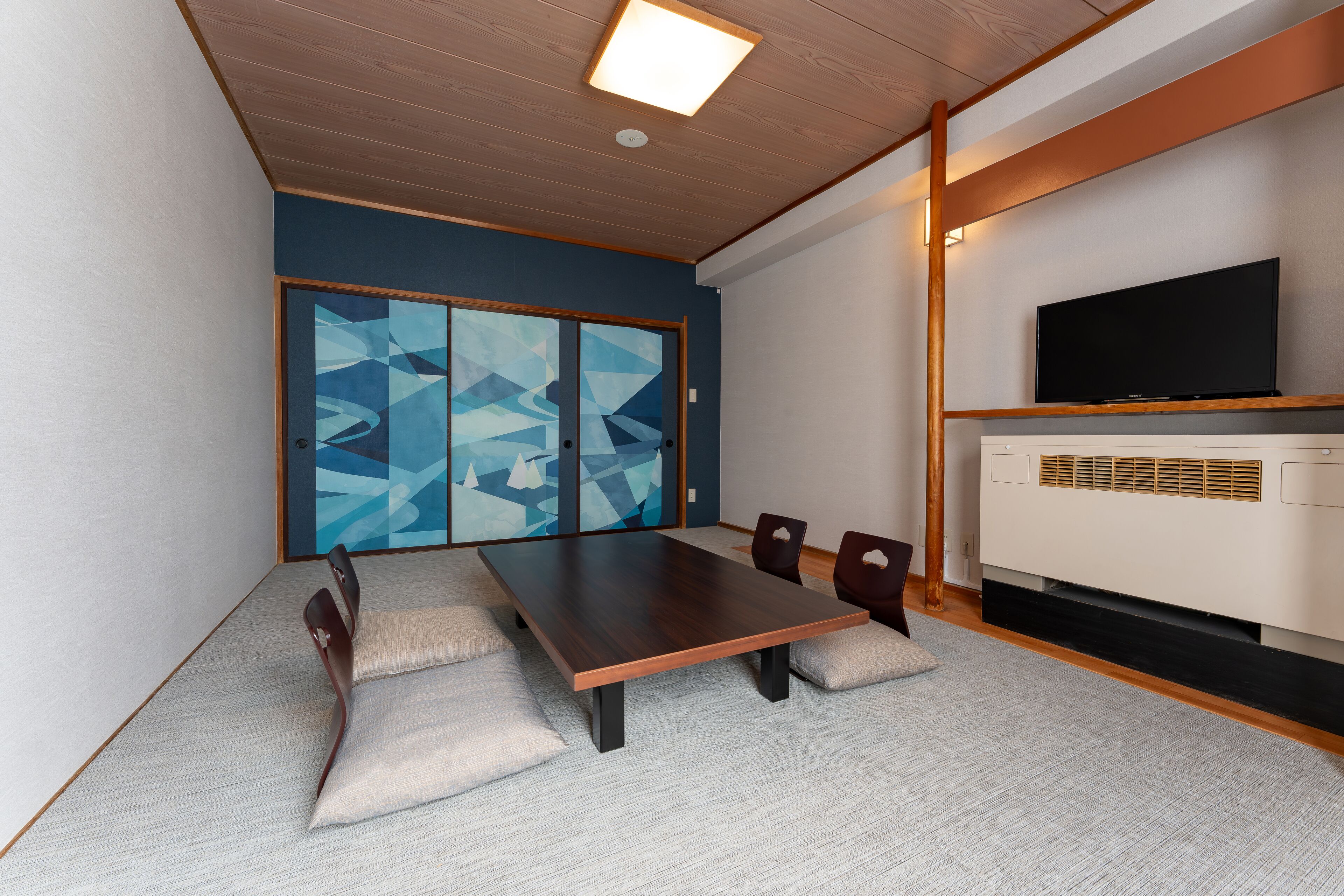 A modern conference room with a long table, cushioned chairs, a flat-screen TV, and a large window with geometric artwork.