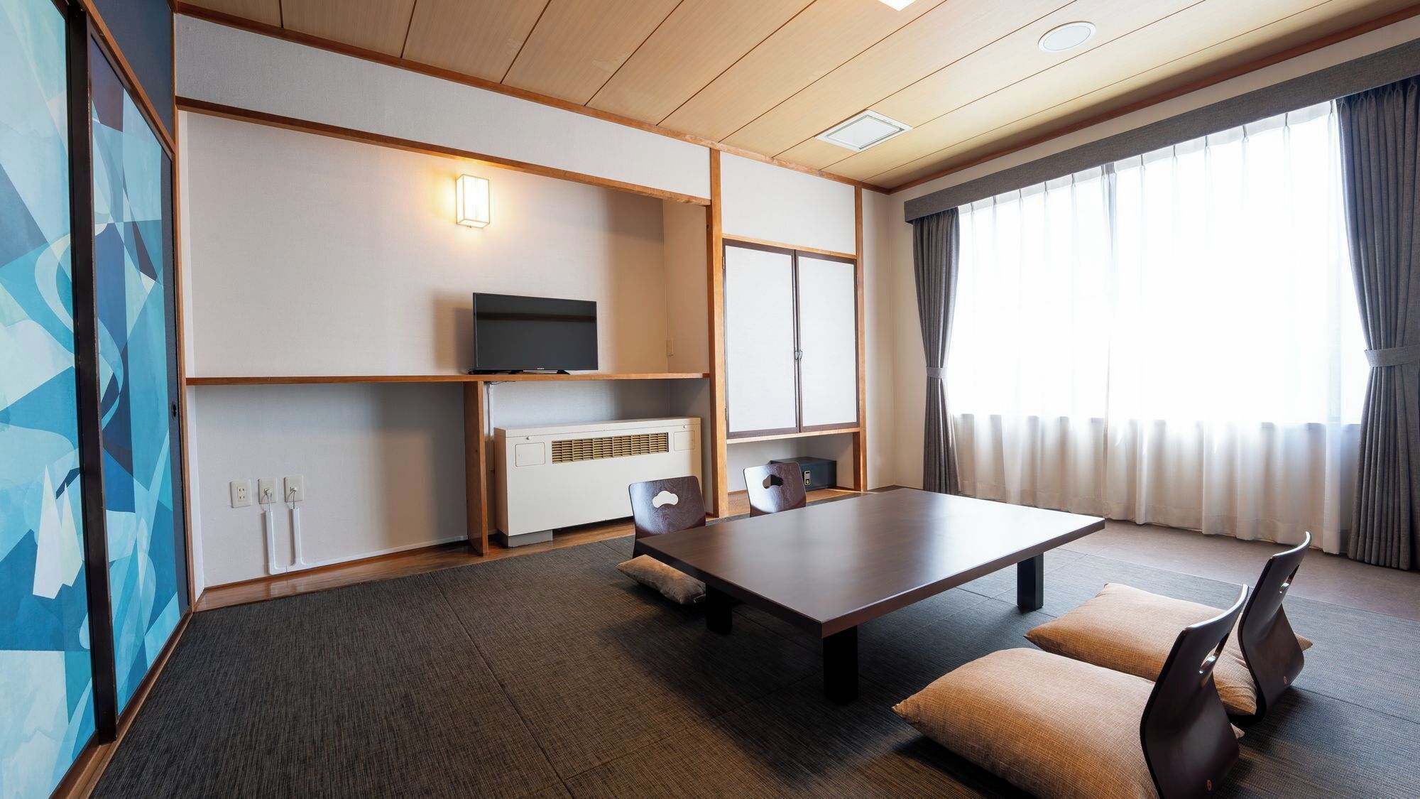 A hotel room with a wooden ceiling, a flat-screen TV, a small heater, a sofa, and a large window with curtains.
