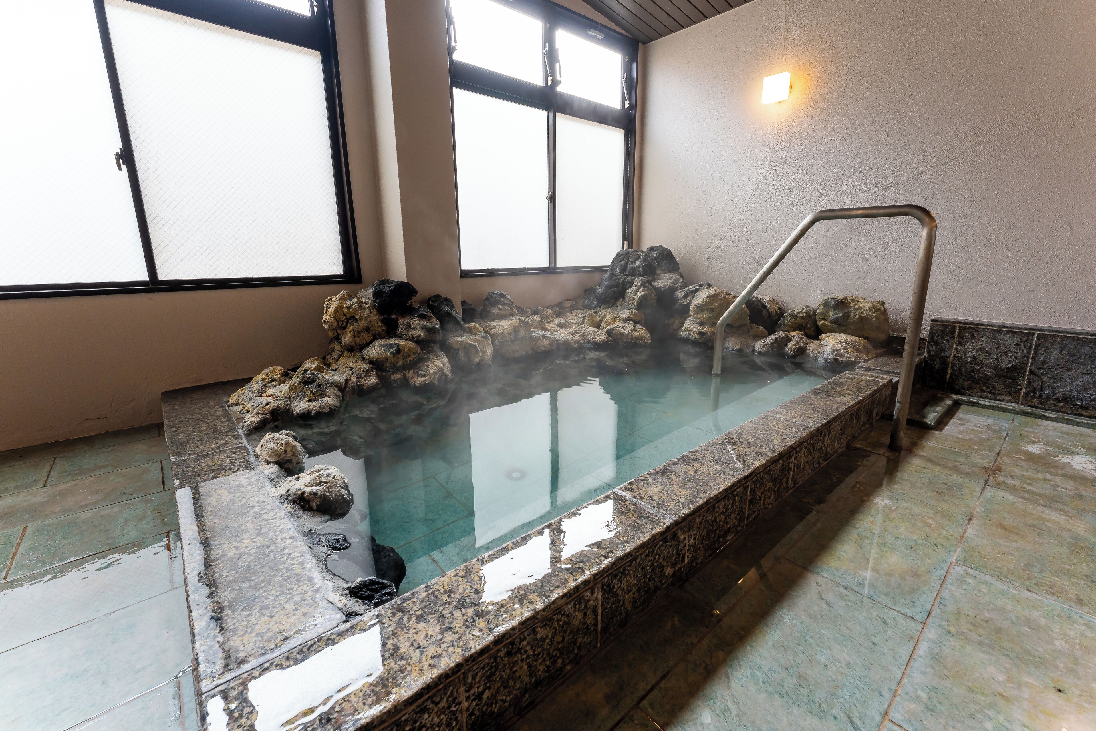 A hot spring bath with a stone edge and a metal ladder, surrounded by rocks.