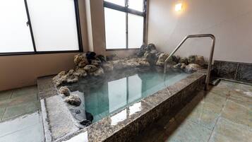 A hot spring bath with a stone edge and a metal ladder, surrounded by rocks.
