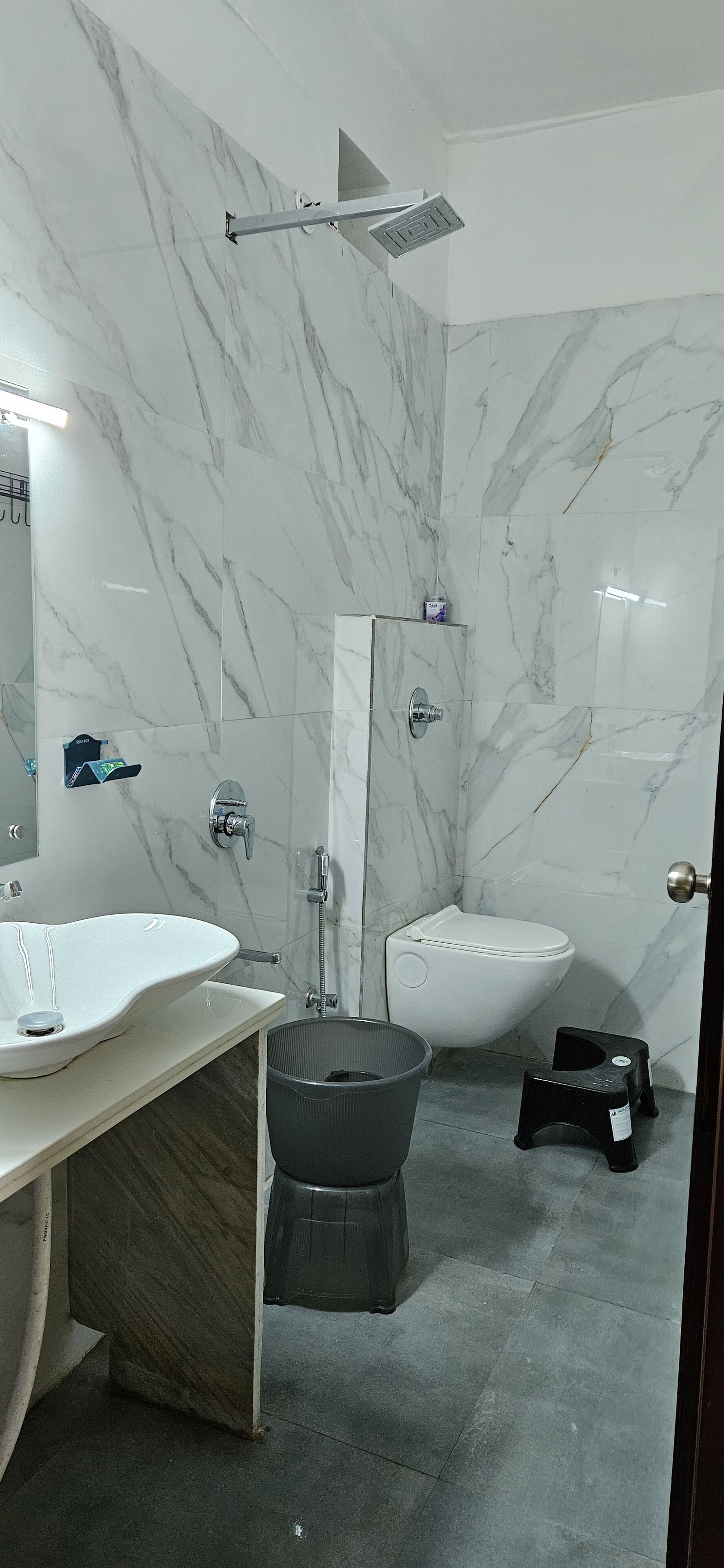 A bathroom with a marble wall, a sink, a toilet, and a shower.