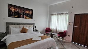 Quarto de hotel com uma cama grande, uma mesa, duas cadeiras, uma porta de madeira e um quadro na parede.
