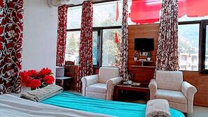 Habitación de hotel con cama, dos sillones, una mesita, televisor y ventana con cortinas.