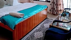 Un dormitorio con cama, ventilador de techo, ventana con cortinas, una mesita y una silla.
