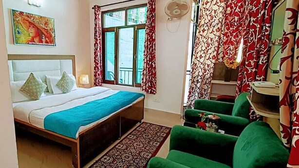 Un dormitorio con cama, sillón verde y una mesita de noche con lámpara.