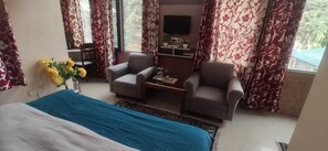 A hotel room with a bed, two armchairs, a coffee table, a TV, and curtains. - Kumar Residency (Dharamshala)