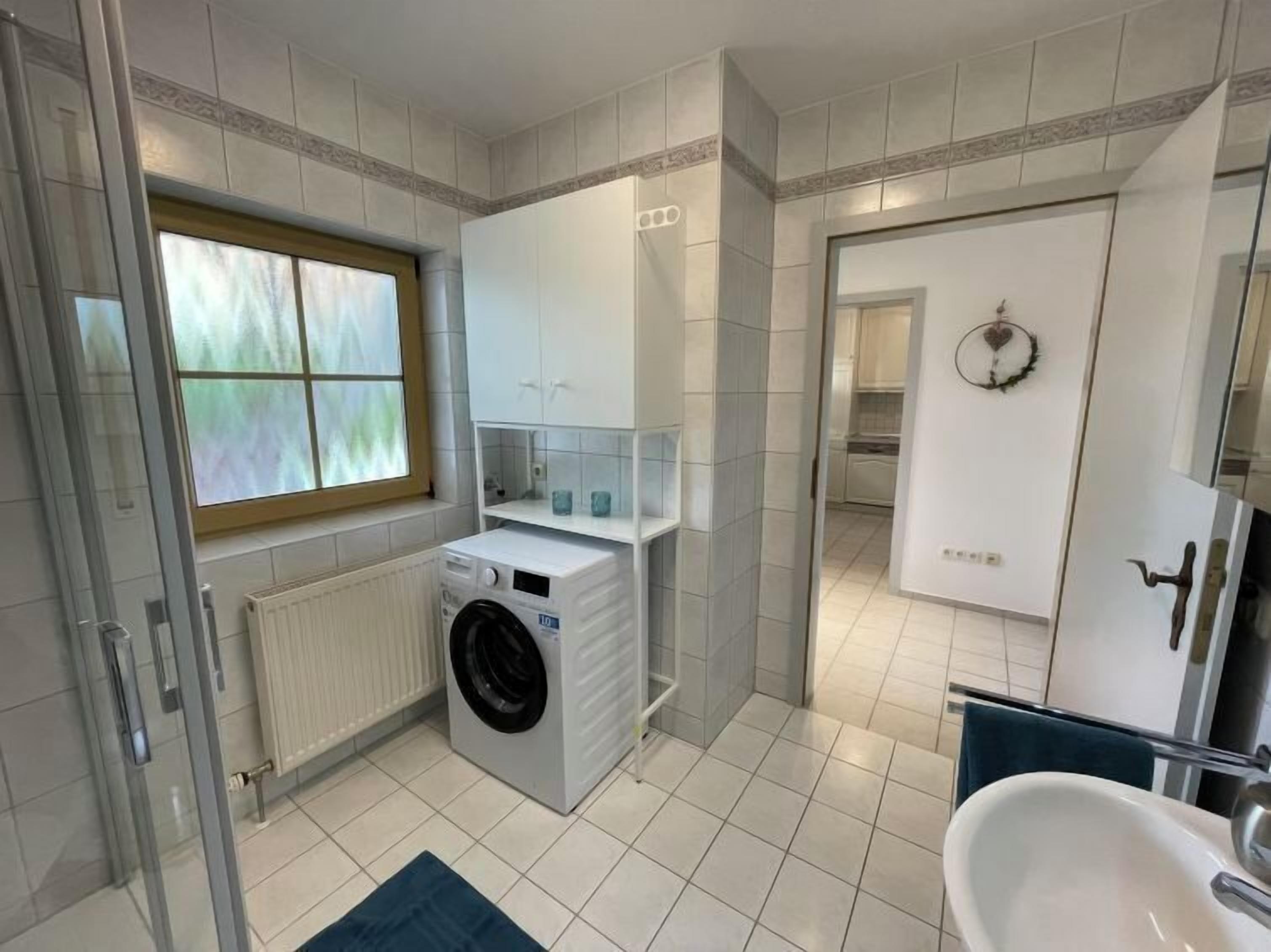 A modern bathroom with a built-in washing machine, a glass shower enclosure, and a sink.
