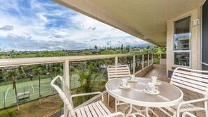 A balcony with a tennis court view, white furniture, and a clear sky.