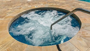 A hot tub with a metal ladder, surrounded by a stone pool area.