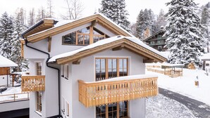 Un chalet à deux étages doté d’un balcon, de grandes fenêtres et d’un toit recouvert de neige.