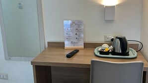A hotel room with a wooden desk, a remote control, a kettle, a tray with a cup and utensils, a trash bin, and a wall-mounted light. - Hotel 26 (Milan)