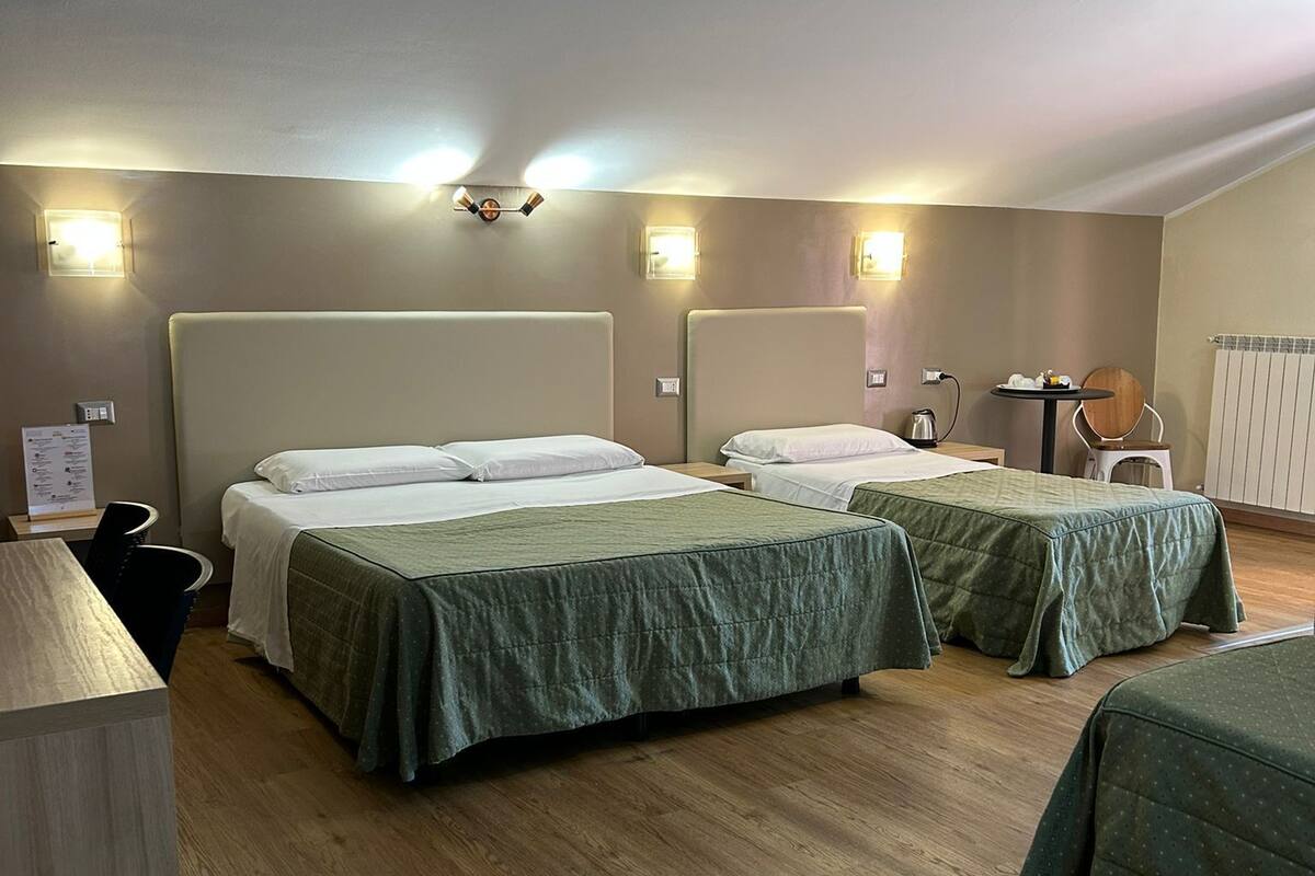 A hotel room with three beds, a wooden floor, and wall-mounted lights.