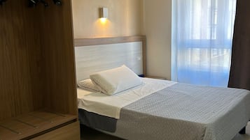 A bedroom with a bed, a wardrobe, a bedside table, a wall-mounted light, and a window with curtains.