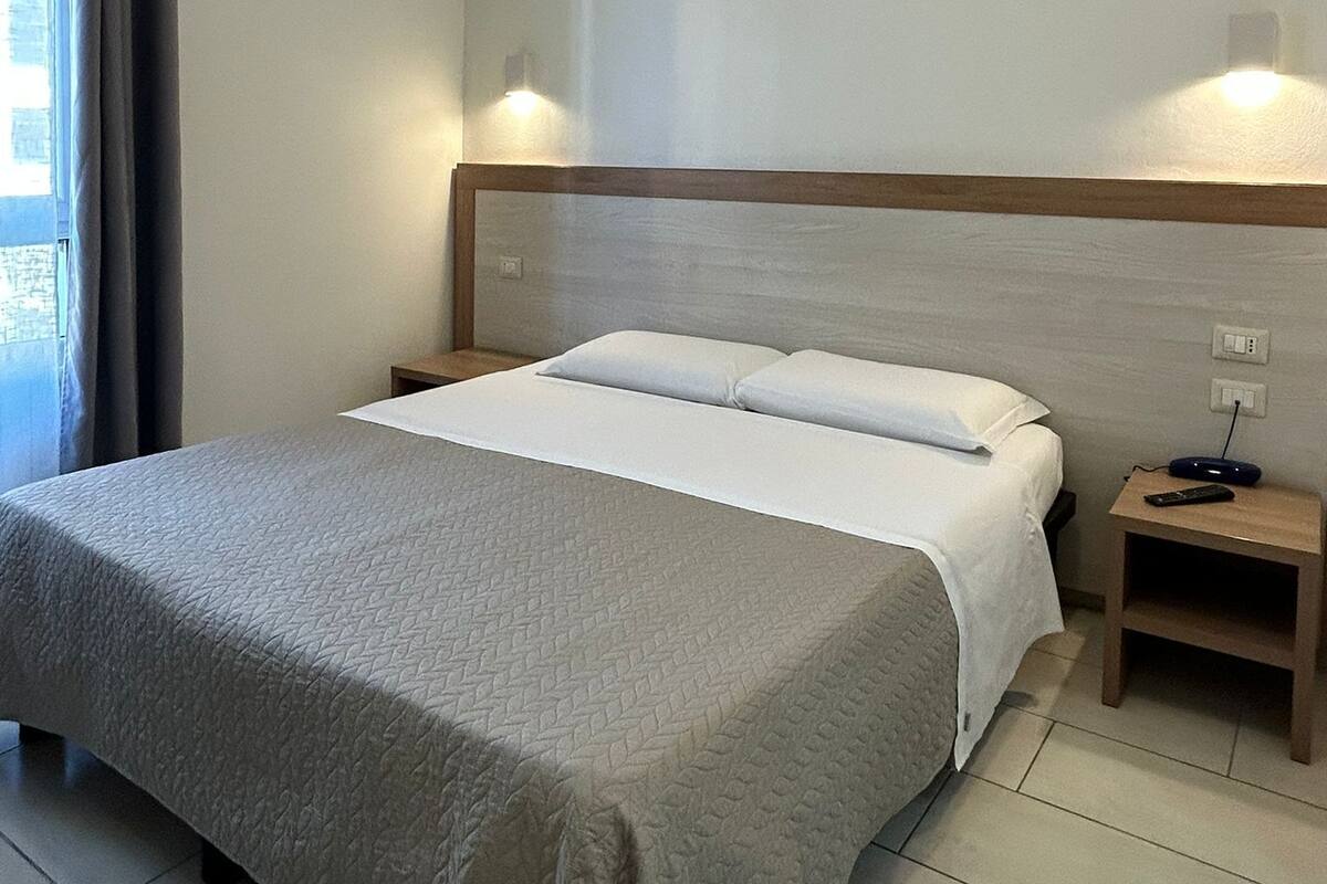 A hotel room with a bed, a nightstand, a lamp, and a window with curtains.