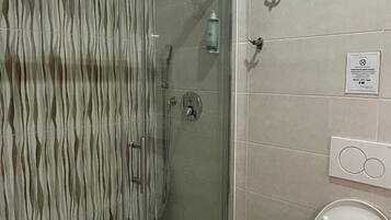 A bathroom with a glass-enclosed shower, a toilet, and a wall-mounted soap dispenser.