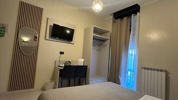 Camera d'albergo con due letti, una TV, una scrivania con sedie, uno specchio, un armadio e un bagno.