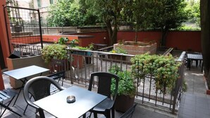 A patio area with tables and chairs, surrounded by potted plants and a metal fence. - Hotel 26 (Milan)
