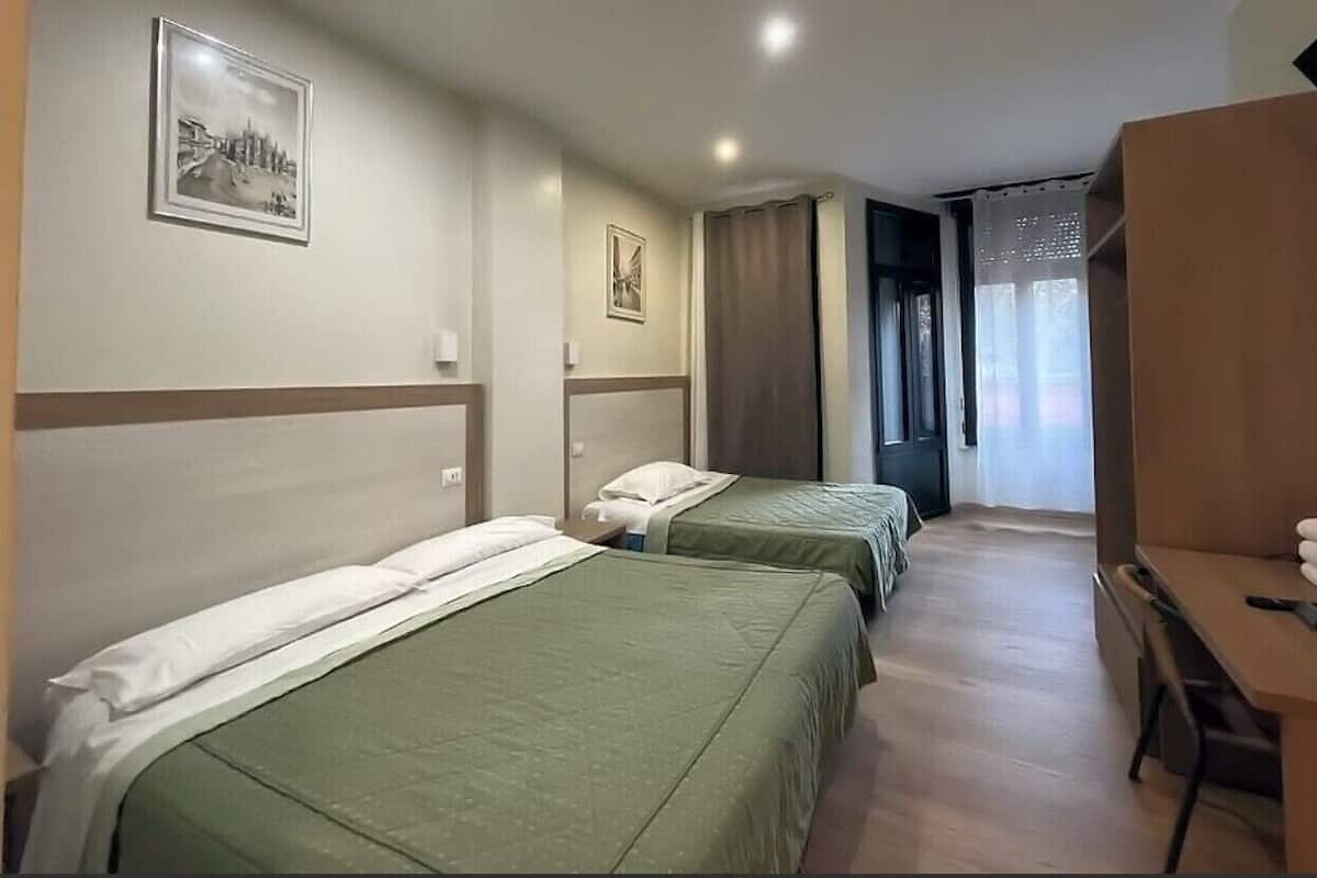 A hotel room with two single beds, a desk, and a chair.