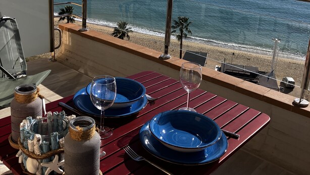 A dining table with blue plates and wine glasses, overlooking a beach and ocean. - BEACH LOFT with fantastic view over the Mediterranean and Palamos. (Sant Antoni de Calonge)