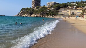 A beach with clear blue water, people swimming and walking along the shore, and buildings in the background. - BEACH LOFT with fantastic view over the Mediterranean and Palamos. (Sant Antoni de Calonge)