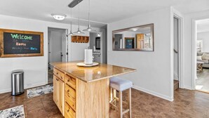 A modern kitchen with a wooden island, pendant lights, and a welcome sign.